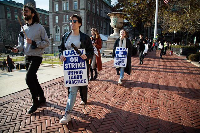 Protesters hold signs saying "UAW on strike" during a protest at Columbia University - one man wears sunglasses and a dark jacket.